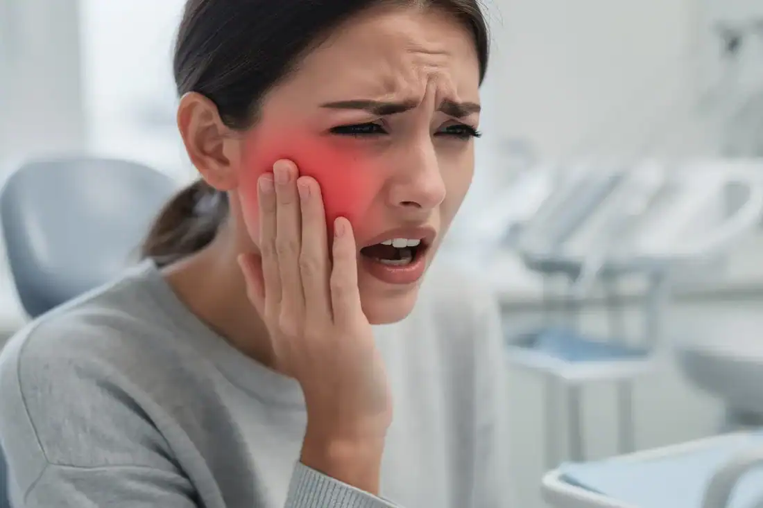 A woman is holding her jaw in discomfort