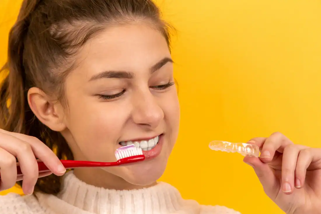 smiling girl in white sweater holding red and white toothbrush