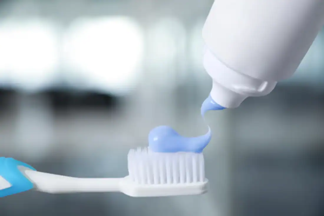 Squeezing toothpaste onto toothbrush against blurred background