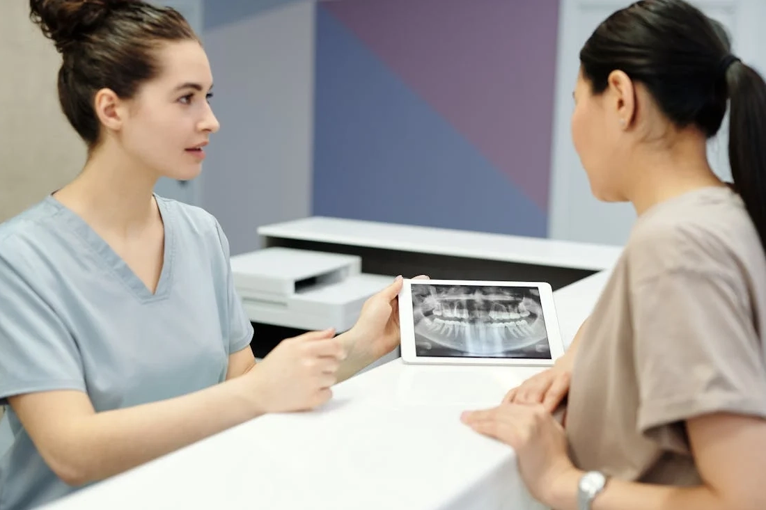 A dentist explains X-ray results to a patient using a tablet in a modern dental clinic.