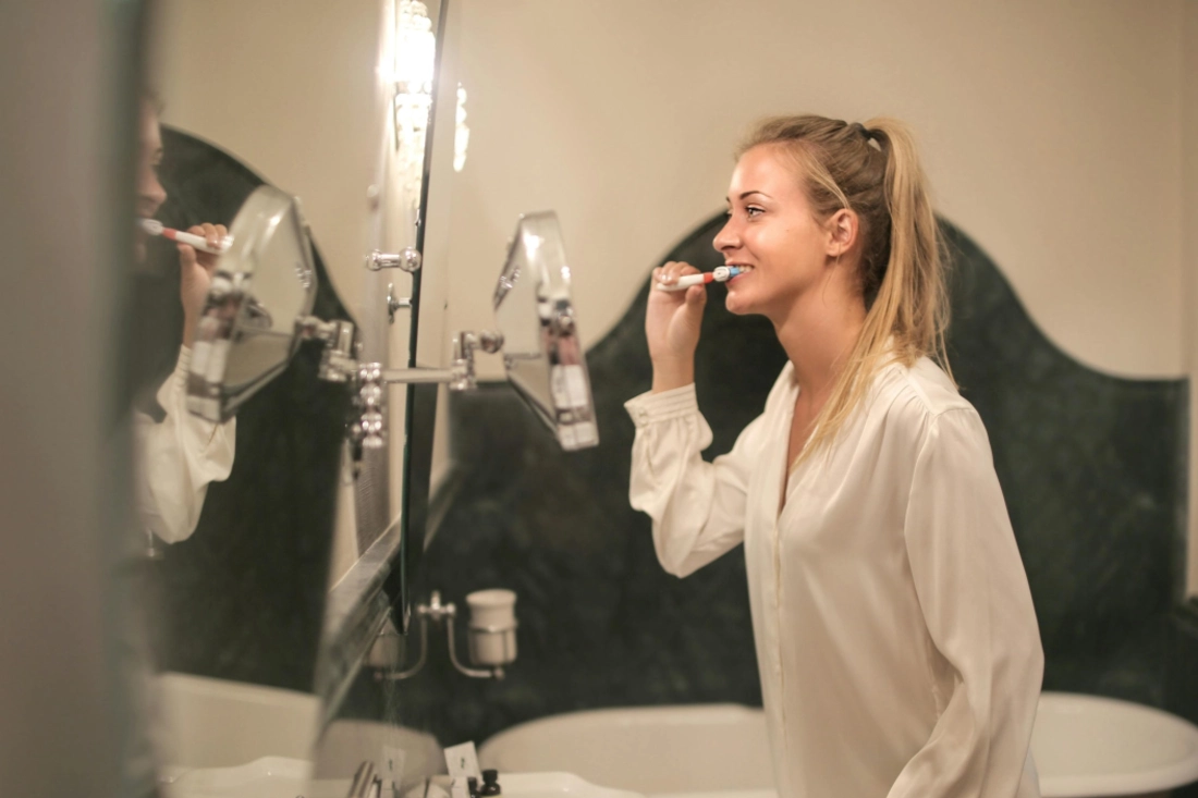 woman brushing her teeth in front of a mirror.