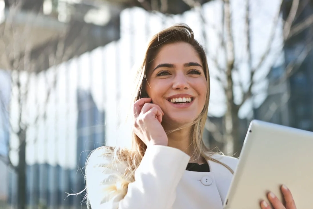 Confident woman using her tablet and phone, smiling outdoors in sunlight.