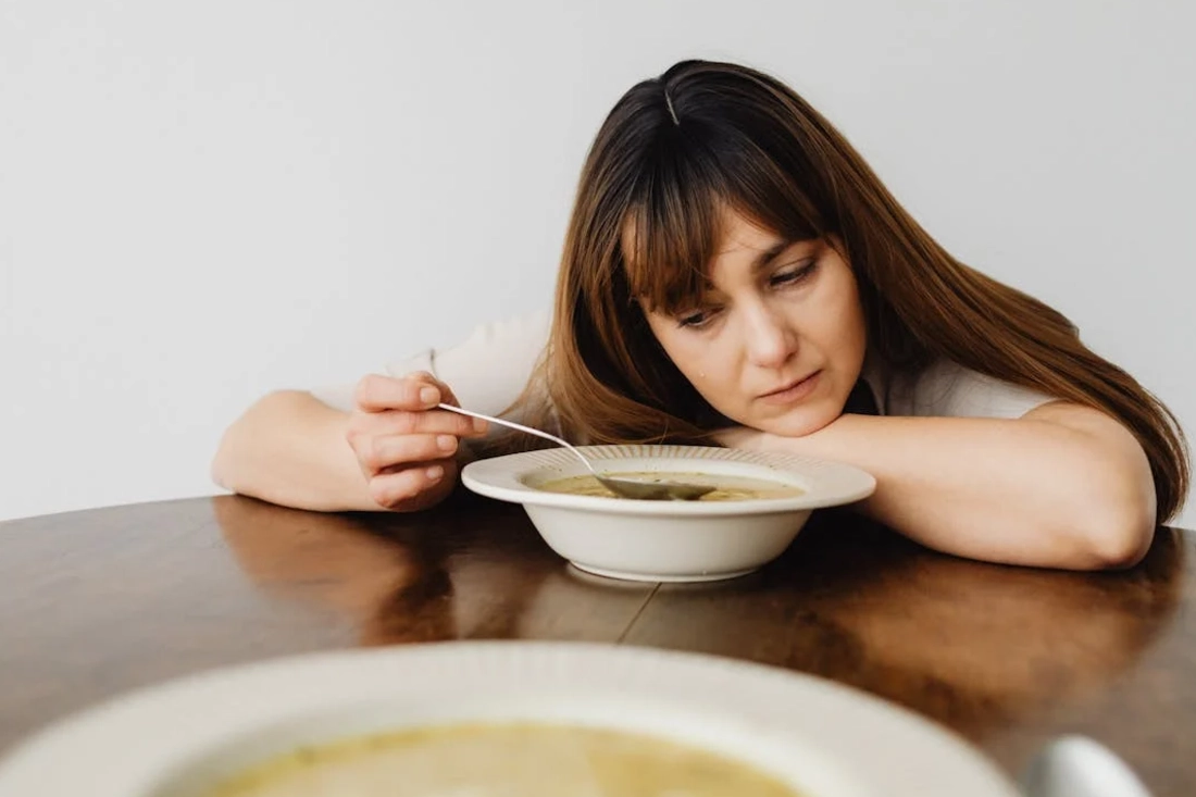 Woman slowly eating soup at a wooden table.